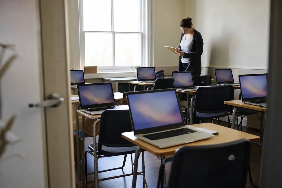 Teacher with a clipboard checking a room of laptops set up for a pilot class