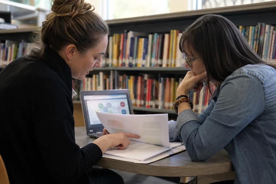 Literacy coach and school librarian comparing a reading program renewal quote at a library table